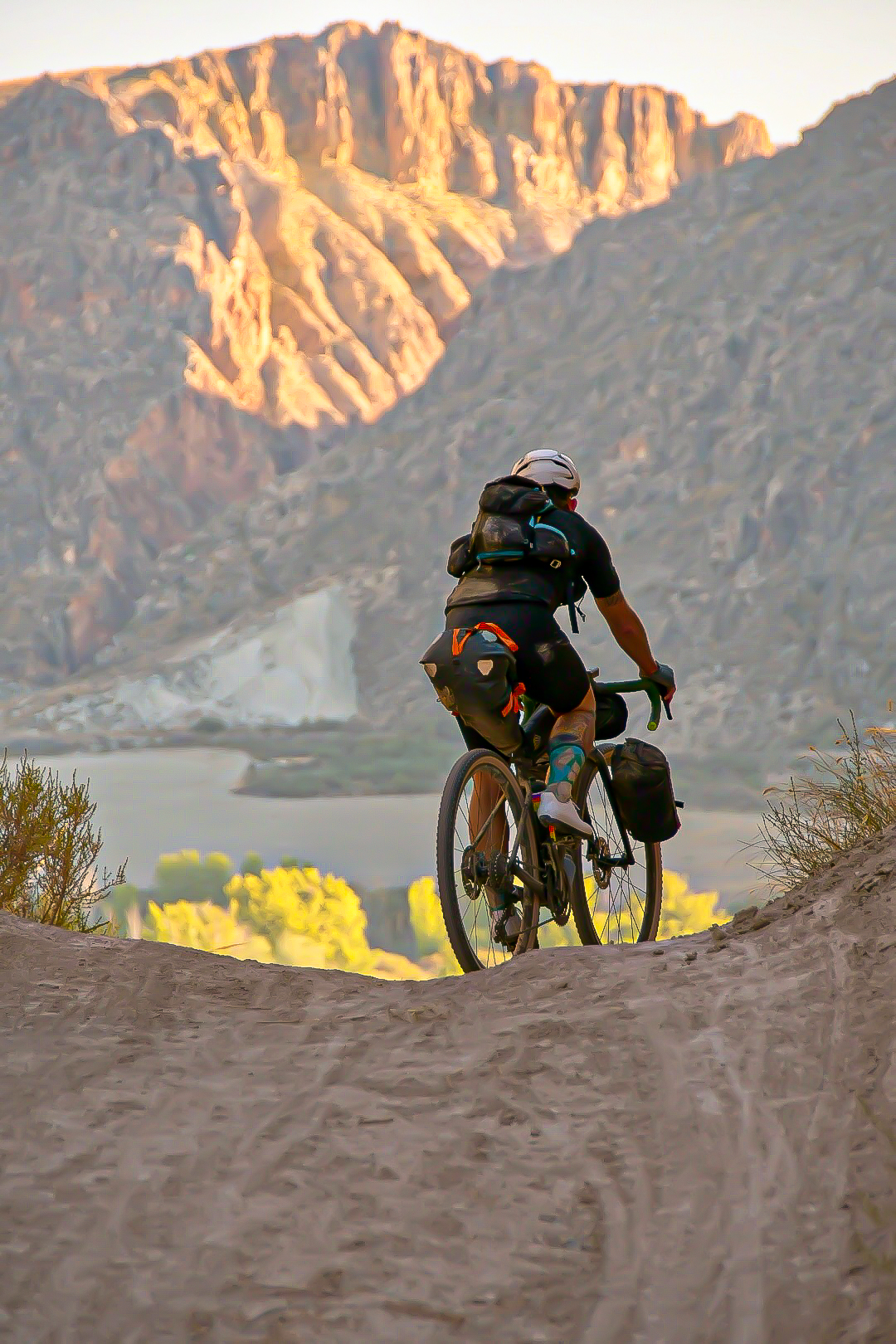 Bikepacker cresting a gravel climb at sunrise above a lake
