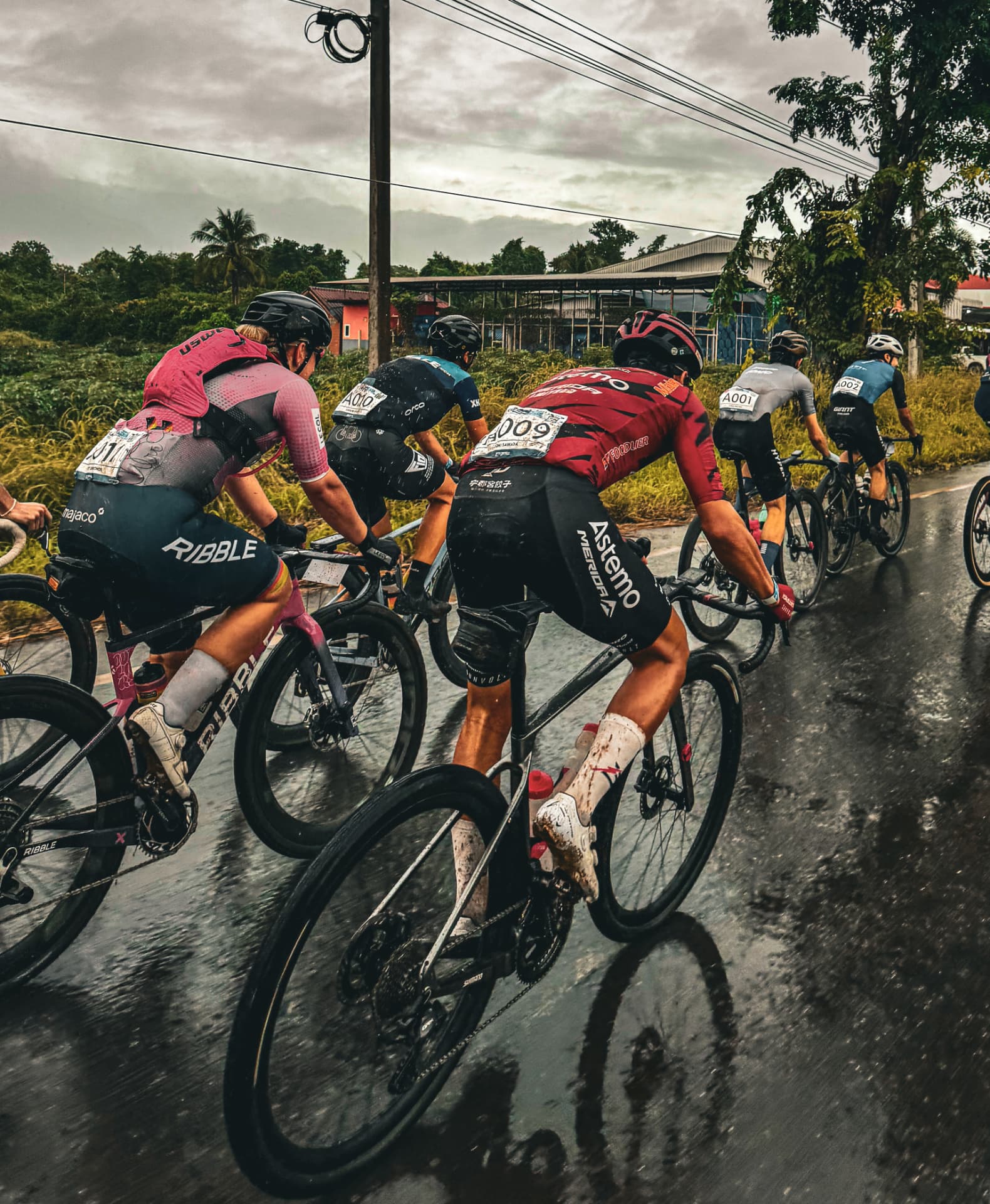 Gravel racers riding in line on a wet tropical road under storm clouds