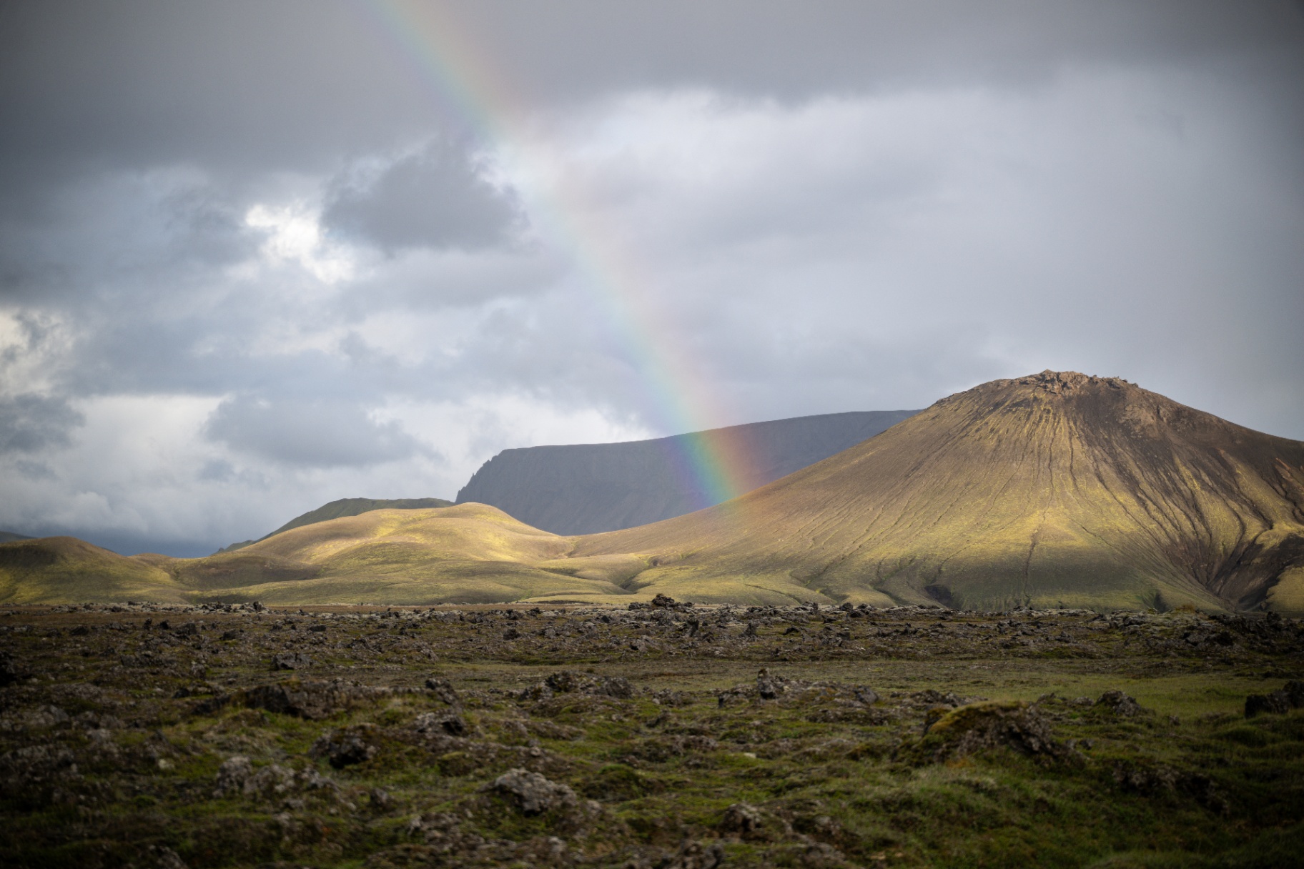 Rainbow falling across a moss covered volcanic cone in the Icelandic highlands