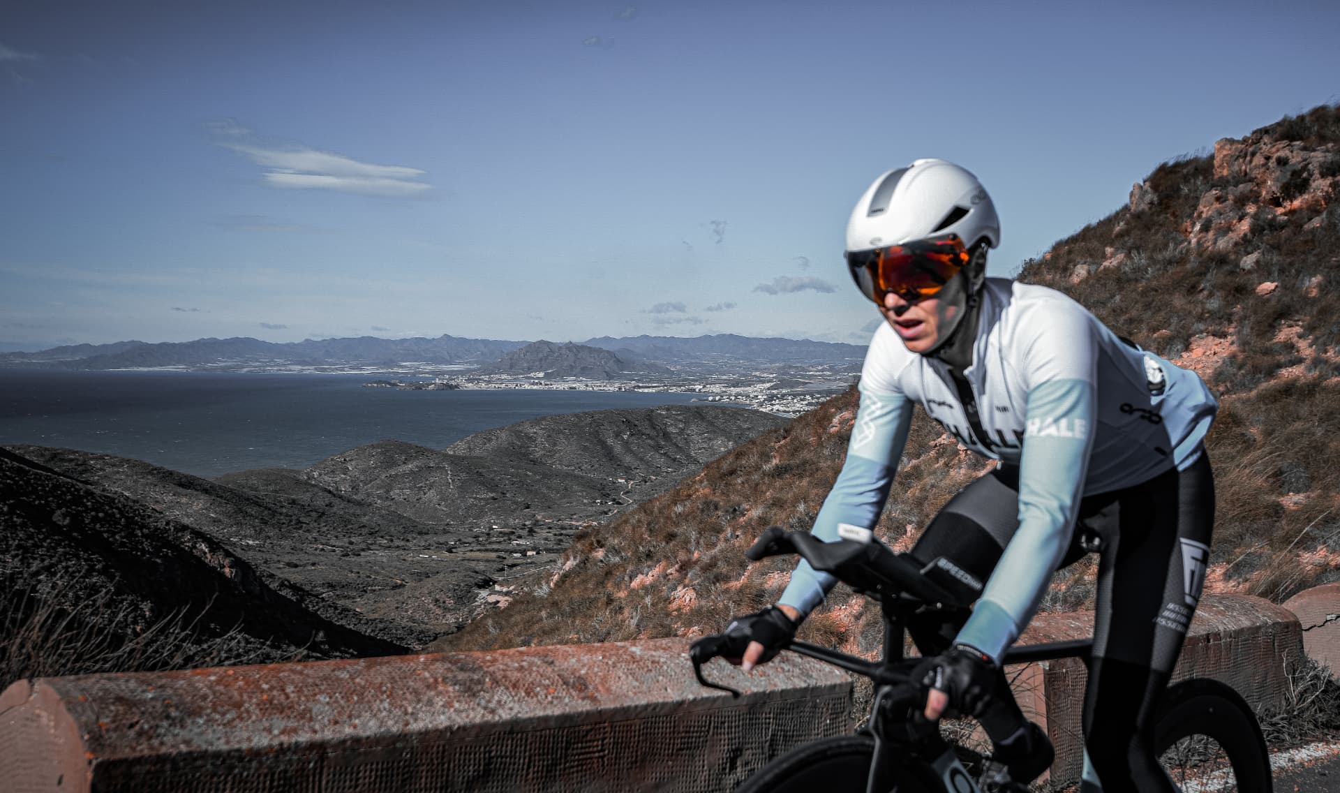 Cyclist climbing a coastal road above a wide bay