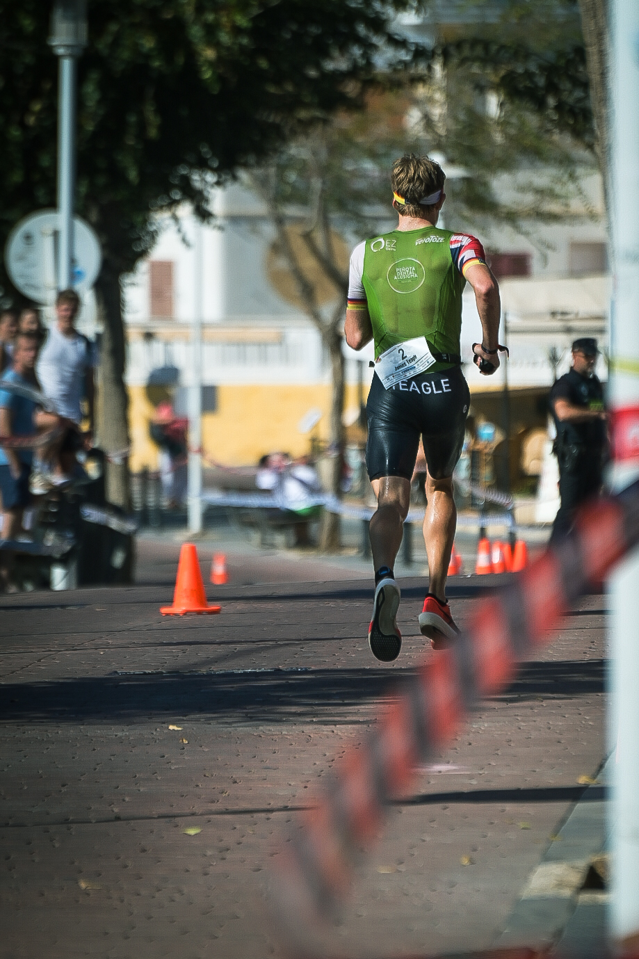 Lead triathlete in a green tri suit running away through a town square