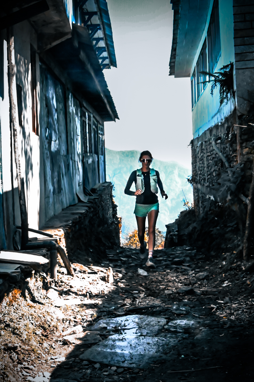 Trail runner descending a shaded stone alley in a Himalayan village
