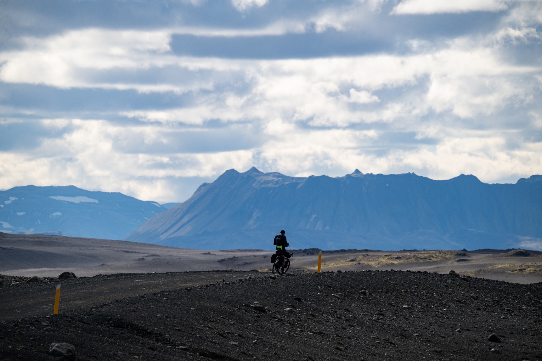 Silhouetted bikepacker on a gravel road with jagged Icelandic peaks beyond