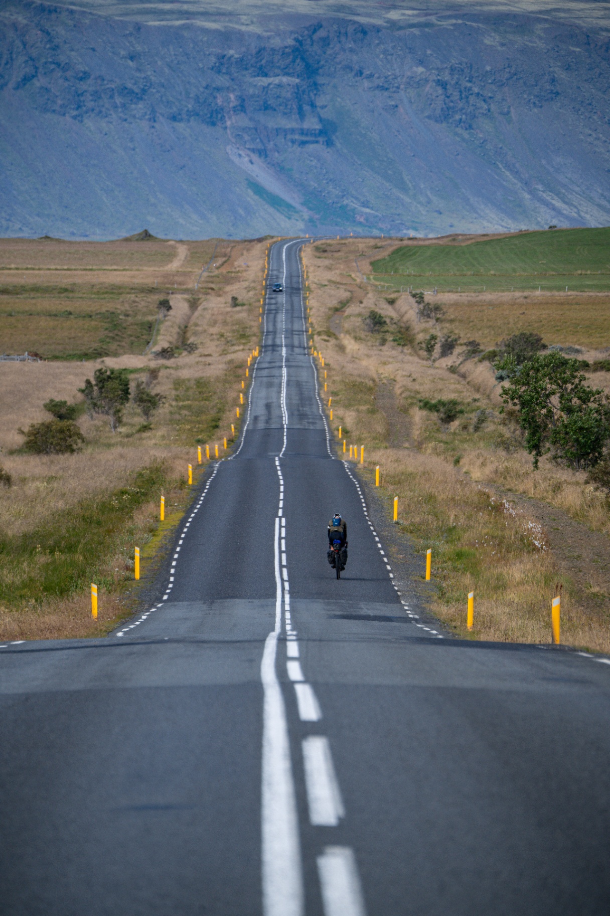 Solo bikepacker riding a dead straight Icelandic road towards a huge mountain wall