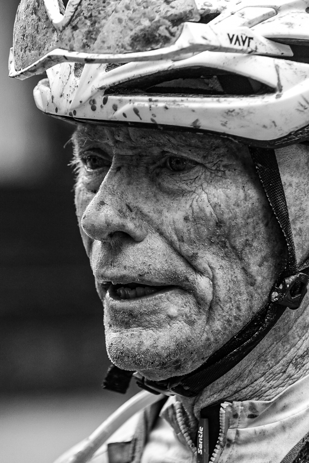 Black and white portrait of a mud covered veteran rider in a scuffed helmet