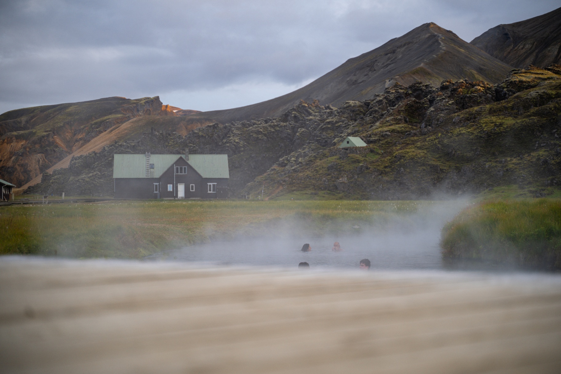 Bathers in a steaming natural hot river beside a highland hut