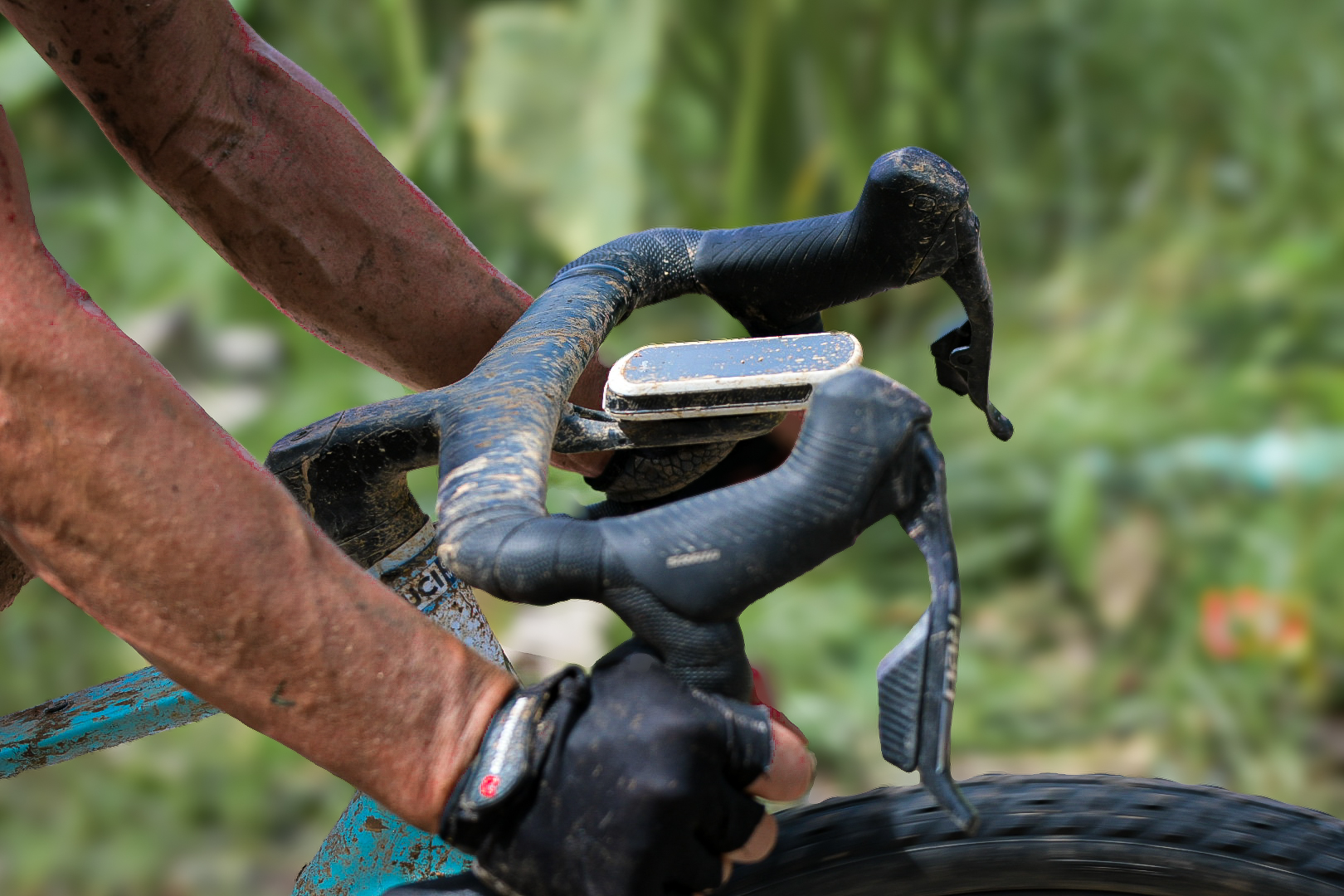 Detail of dusty hands on drop handlebars during a gravel stage