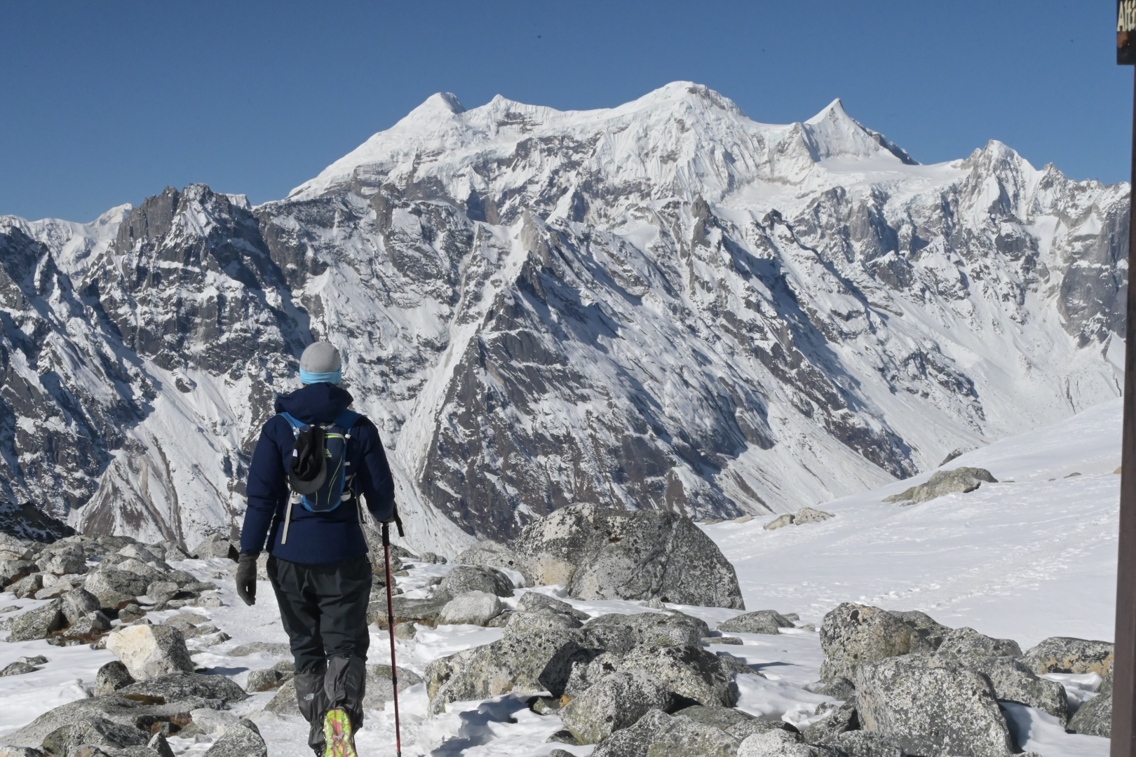 Hiker crossing snow-covered boulders below a Himalayan peak