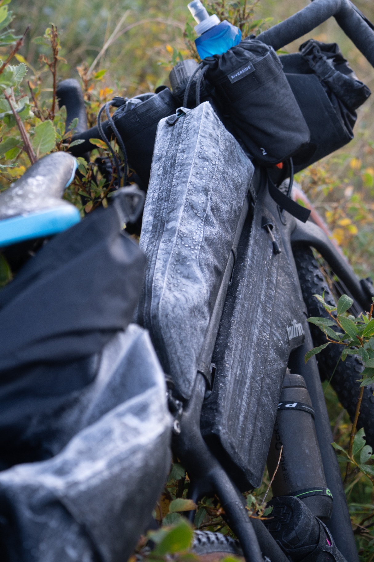 Rain beaded bikepacking bags and frame pack on a loaded gravel bike in wet scrub