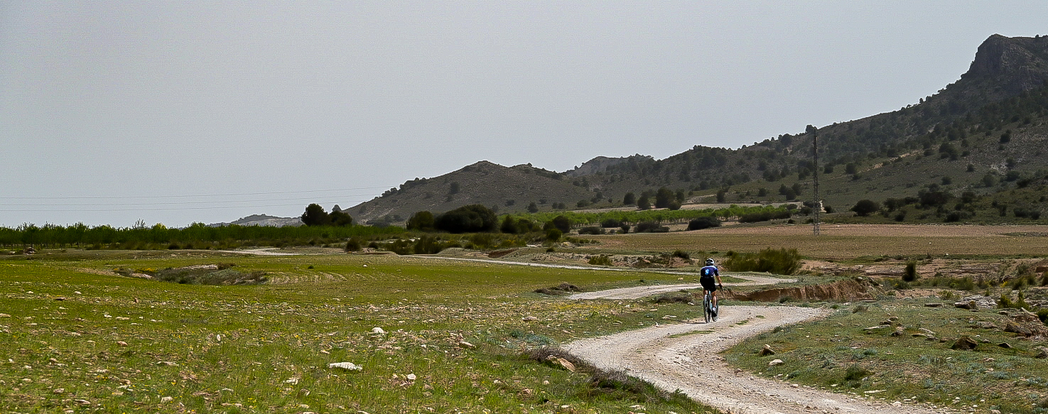 Lone gravel rider on a winding track across open farmland