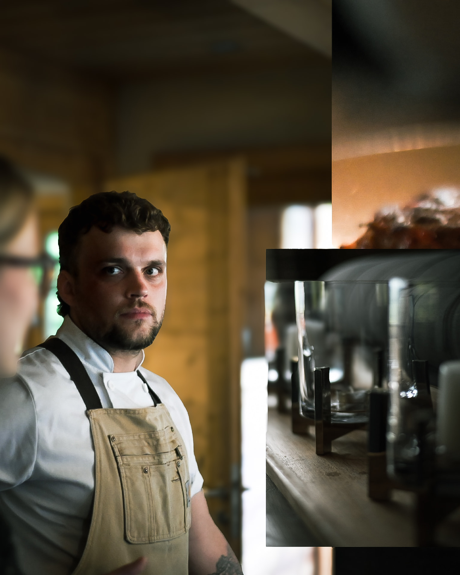 Chef in a canvas apron looking back in a warmly lit kitchen
