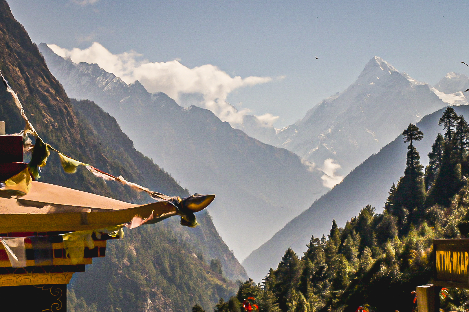 Prayer flags on a monastery roof with hazy Himalayan peaks beyond