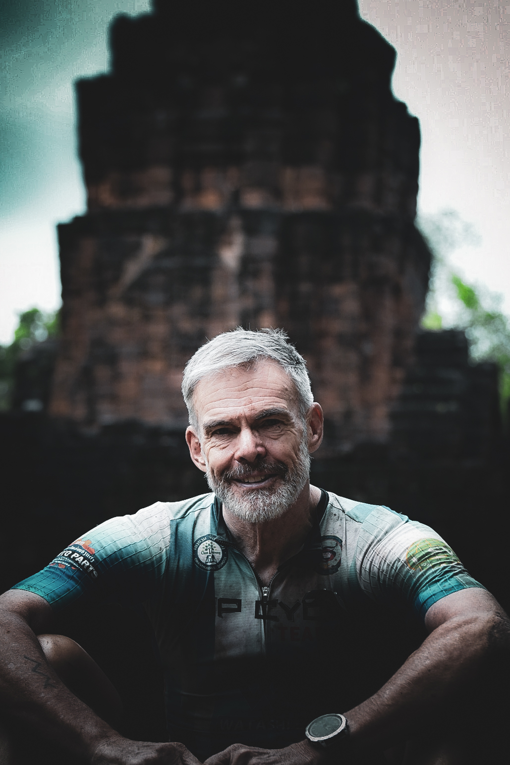 Cyclist in a teal jersey resting in front of an ancient brick temple