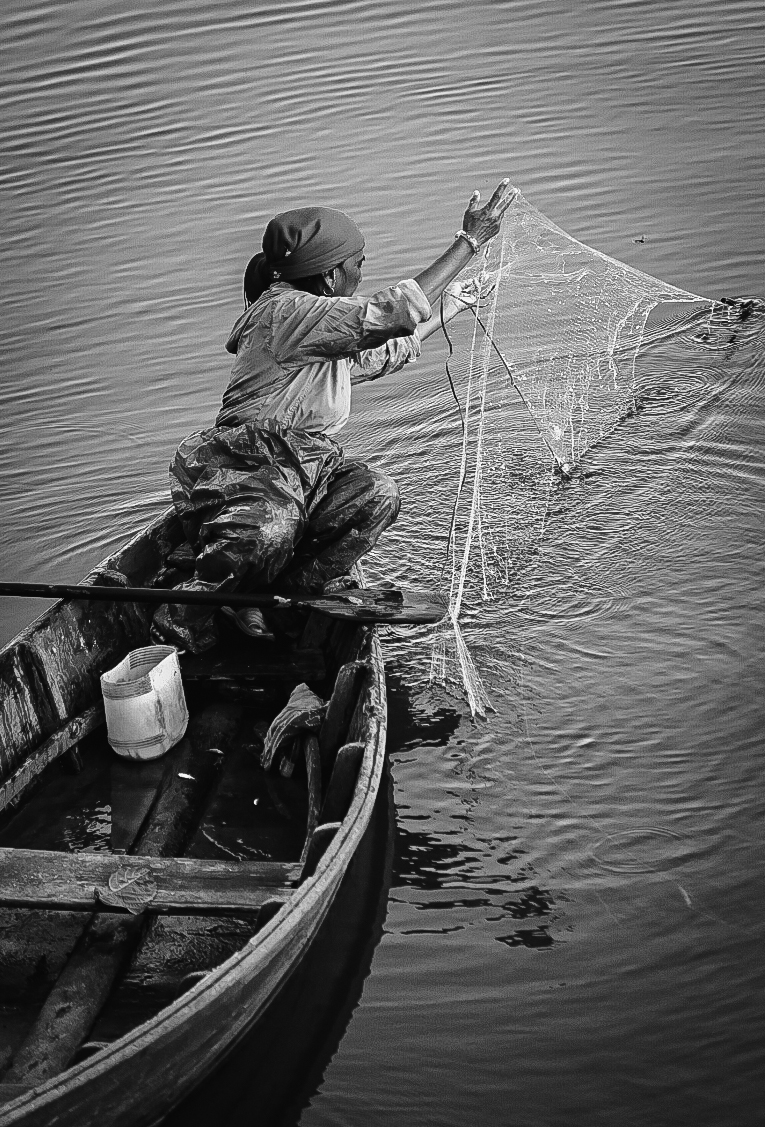 Fisherwoman casting a net from a wooden boat, black and white