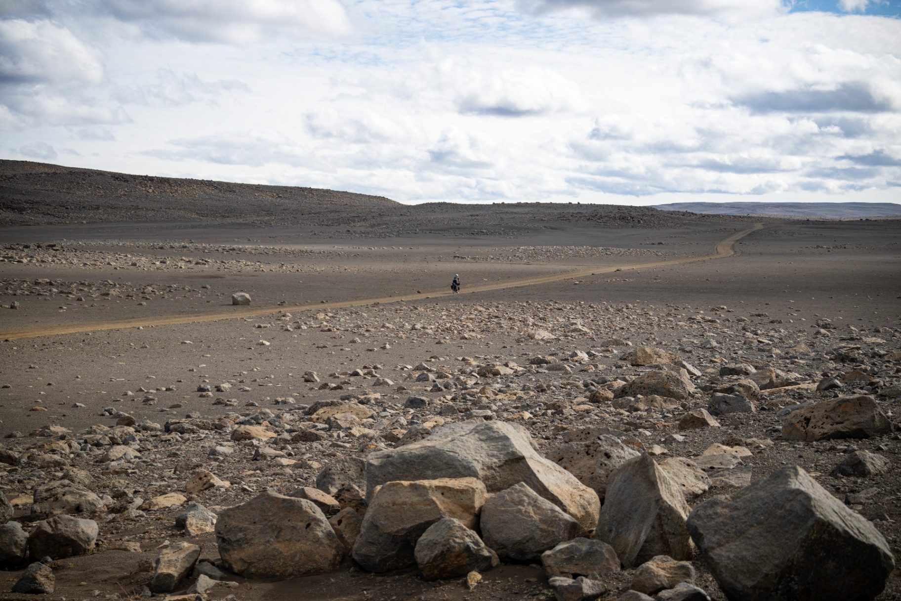 Lone rider crossing a vast grey boulder desert under a big cloud sky