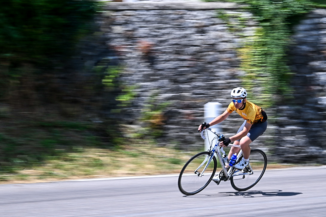 Panned shot of a rider in a yellow jersey against a stone wall
