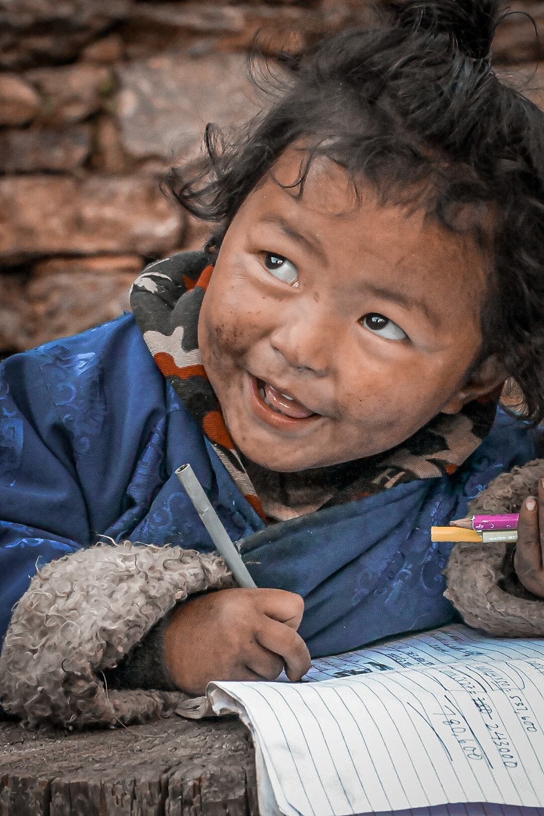 Young child in a blue robe grinning while writing in a notebook