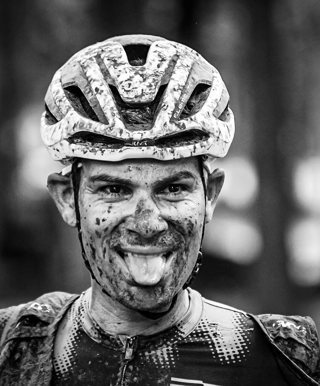 Mud splattered cyclist grinning with his tongue out after a gravel race