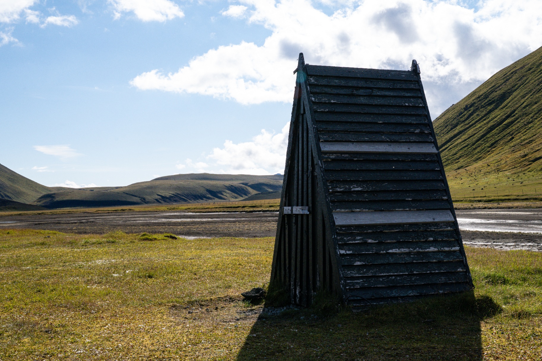 Weathered black timber shelter standing alone on a green highland plain