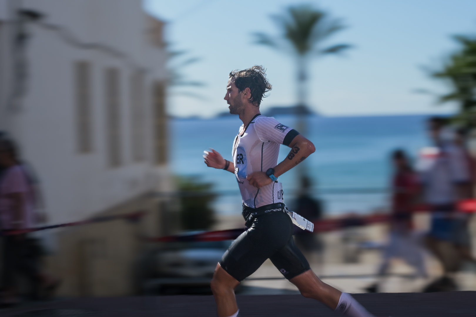 Panned shot of a triathlete running the coastal road past the sea