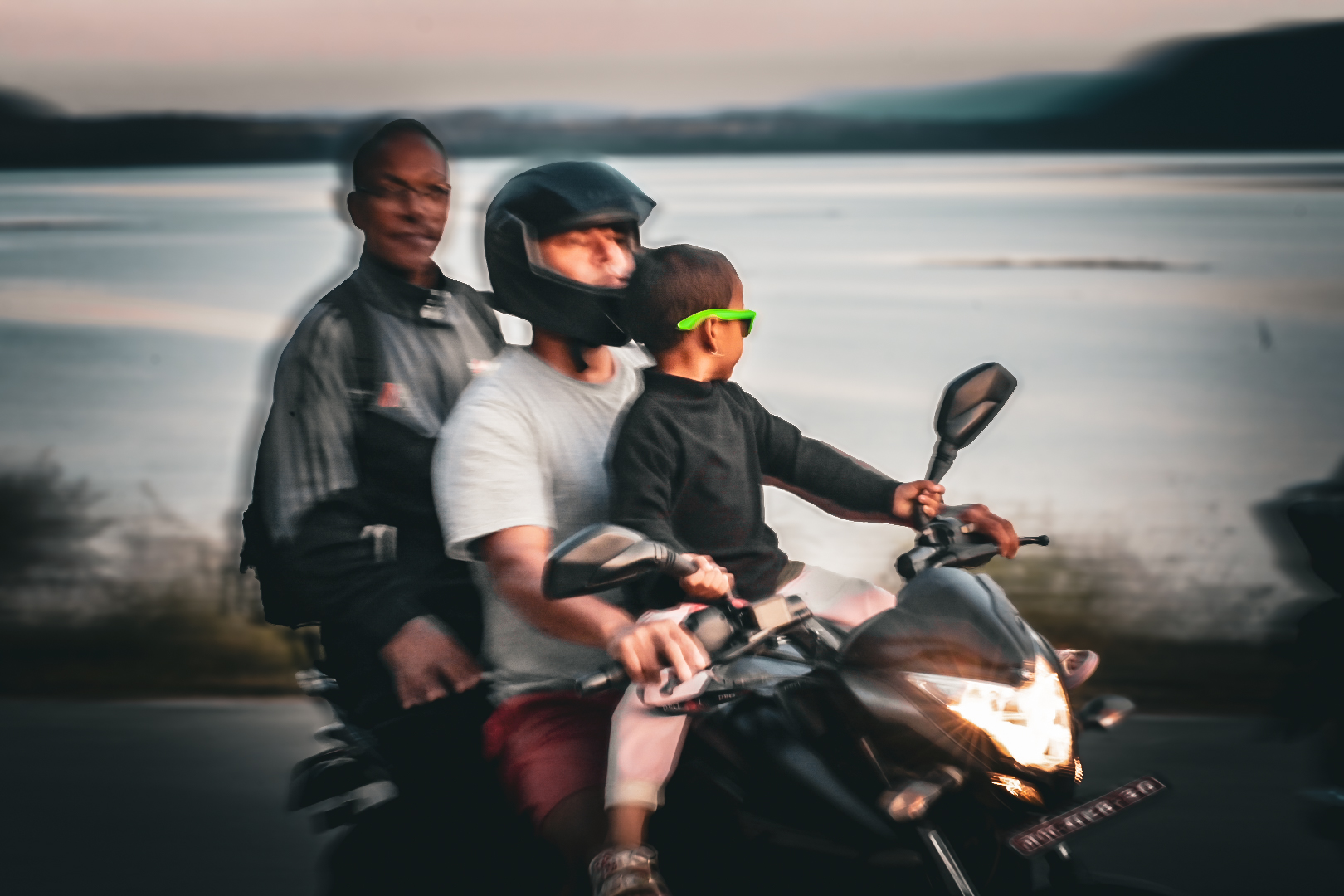 Panned shot of a family riding a motorbike at dusk beside a lake