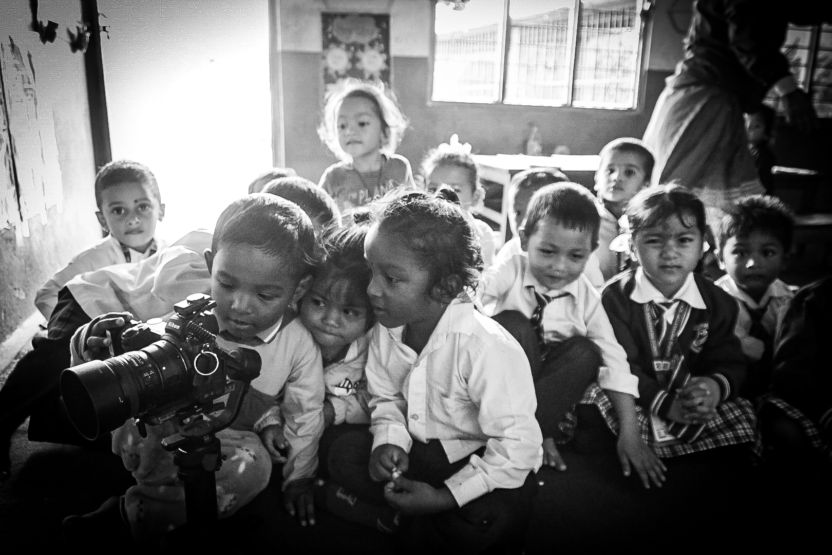 Black and white shot of schoolchildren crowding around a gimbal mounted camera