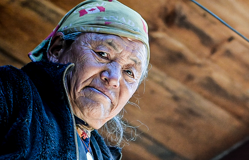 Portrait of an elderly Nepali woman in a headscarf inside a wooden lodge