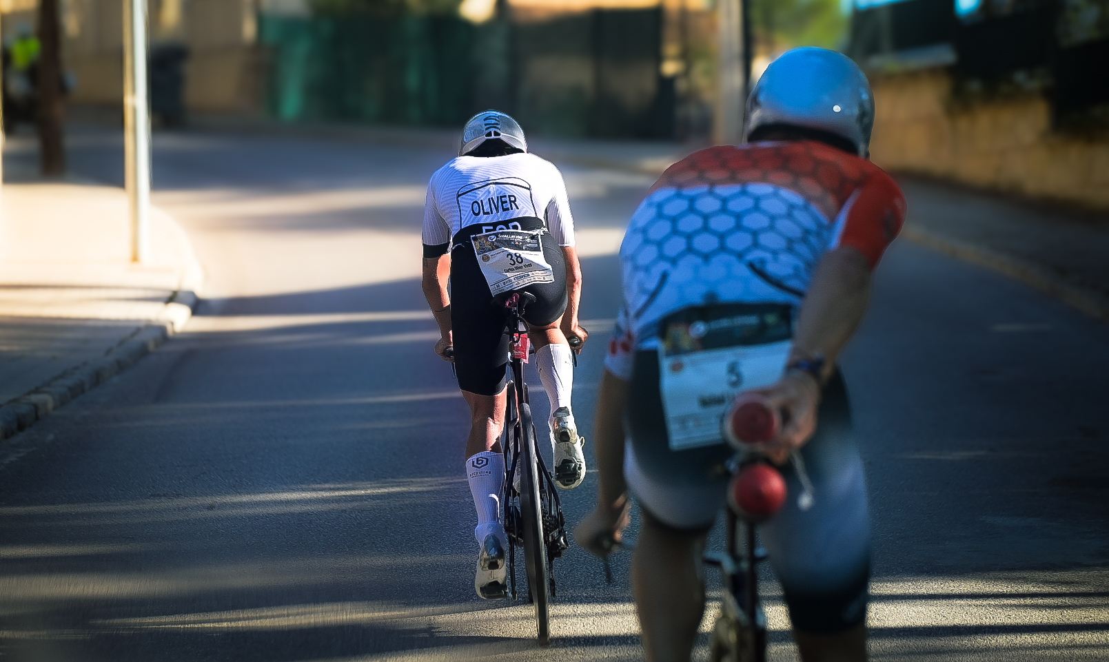 Two triathletes riding away down a sunlit street on the bike leg