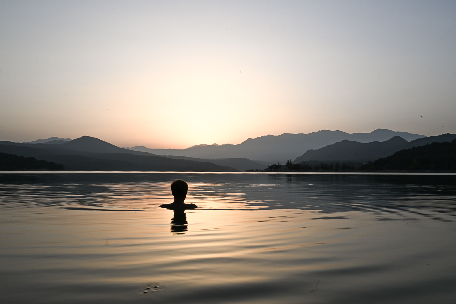 Open water swimmer surfacing on a still lake at sunrise