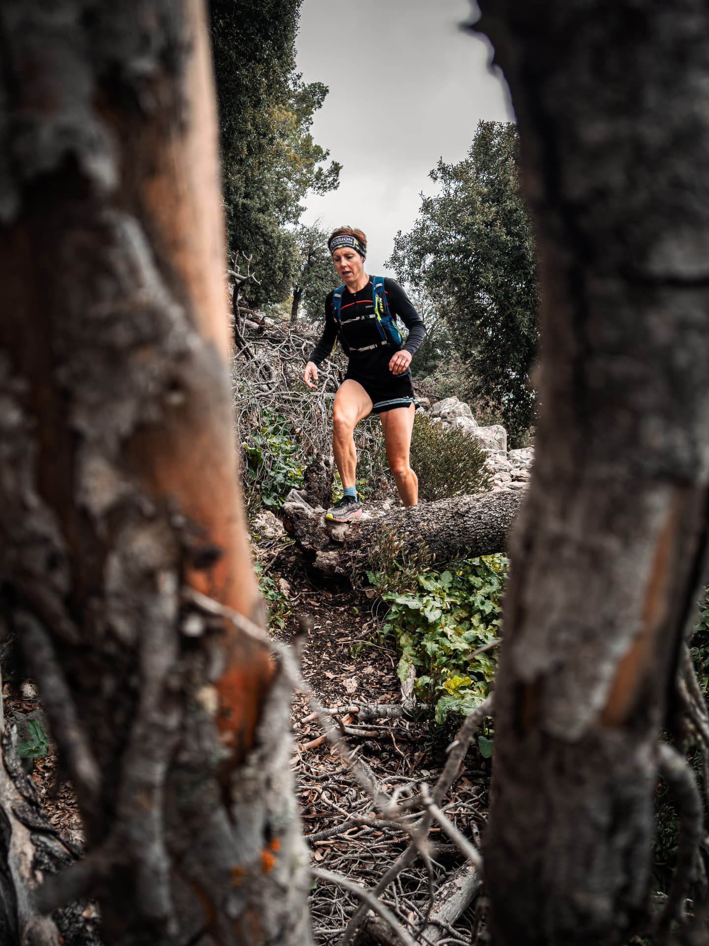 Trail runner descending a wooded slope framed between tree trunks