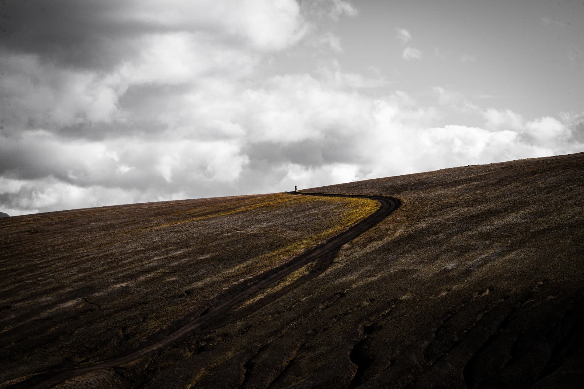 Lone bikepacker on a winding gravel road beneath heavy Icelandic clouds