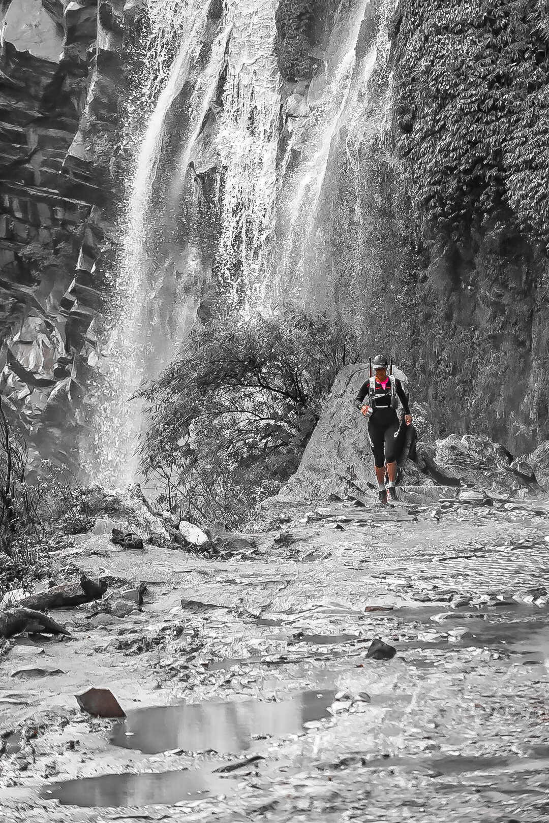 Runner climbing beneath a towering waterfall, desaturated with pink accents