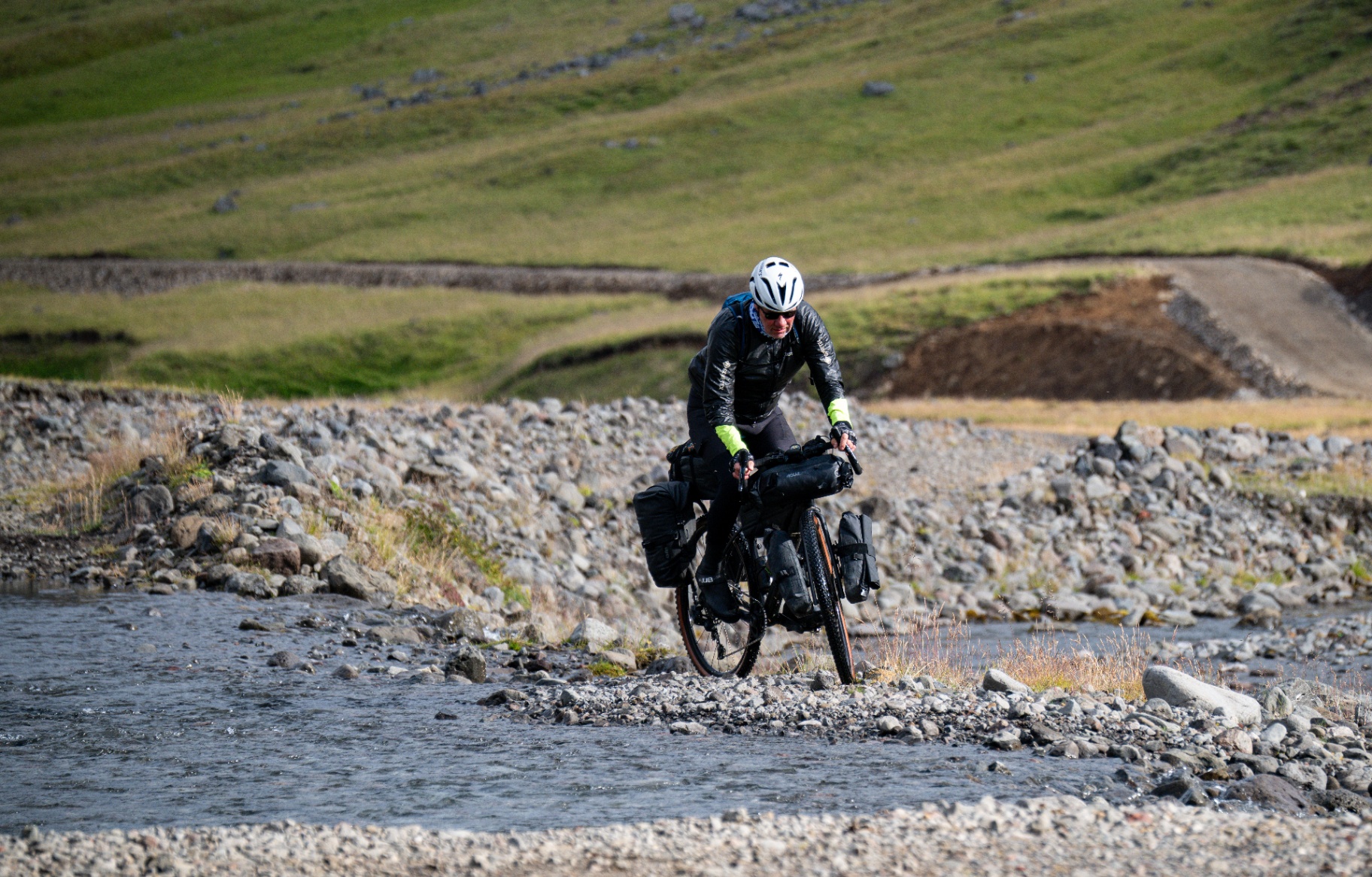 Bikepacker riding out of a river crossing on a stony braided riverbed