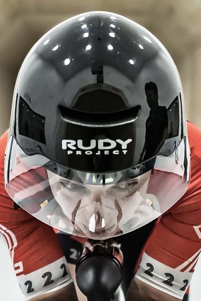 Time trial rider head on, reflections across a black aero helmet