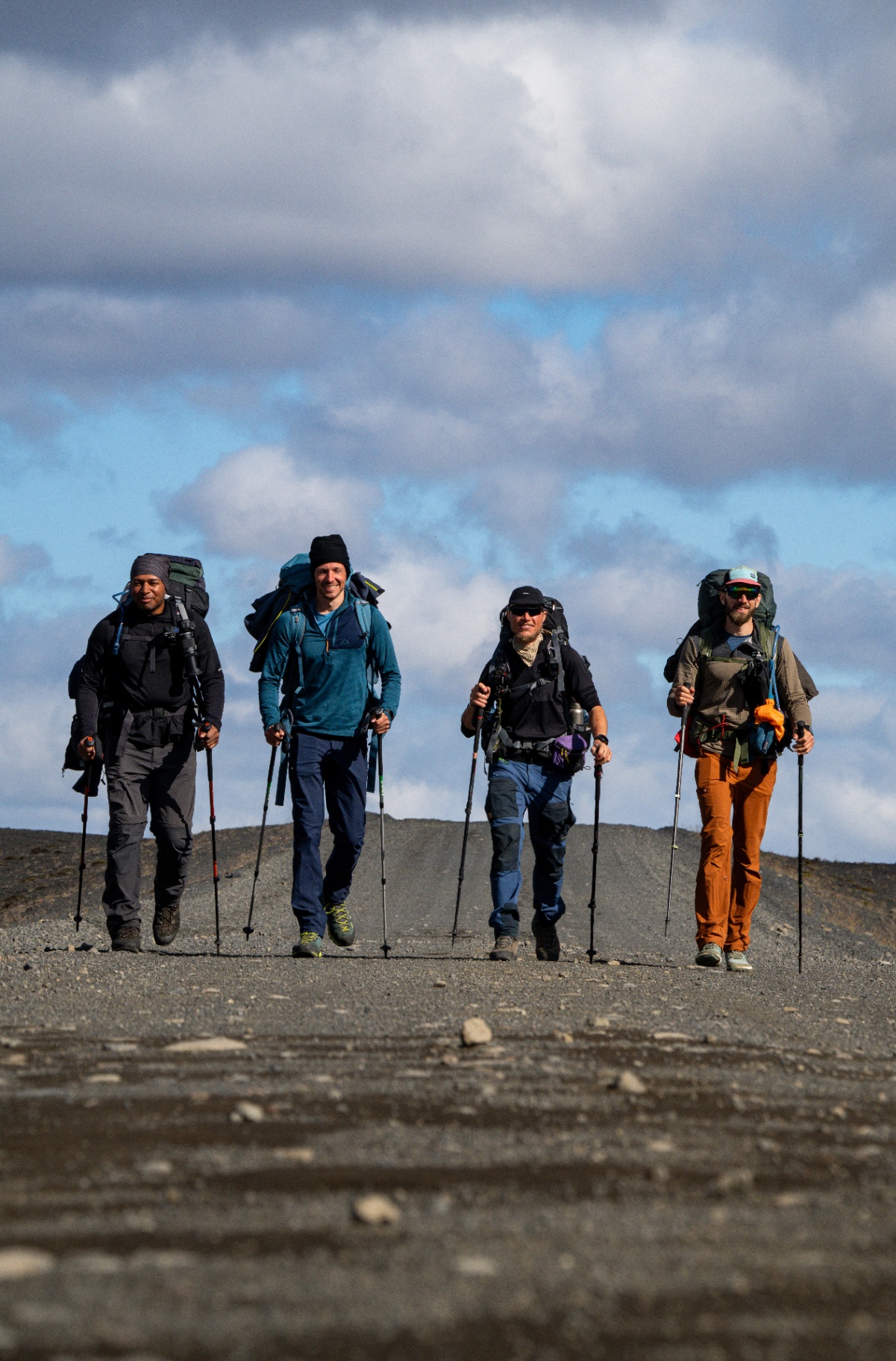 Four trekkers with packs and poles walking towards camera on a highland track