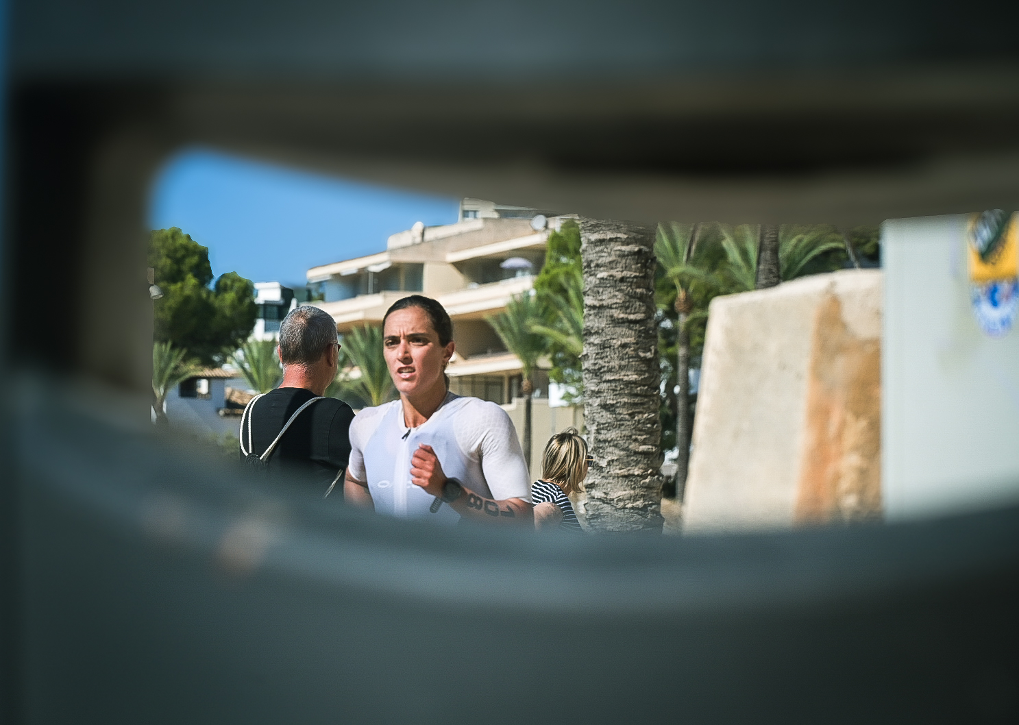 Female triathlete running past spectators, framed through a gap in a wall