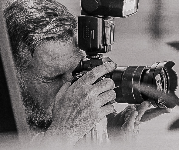 Black and white close up of a photographer working with a flash mounted camera