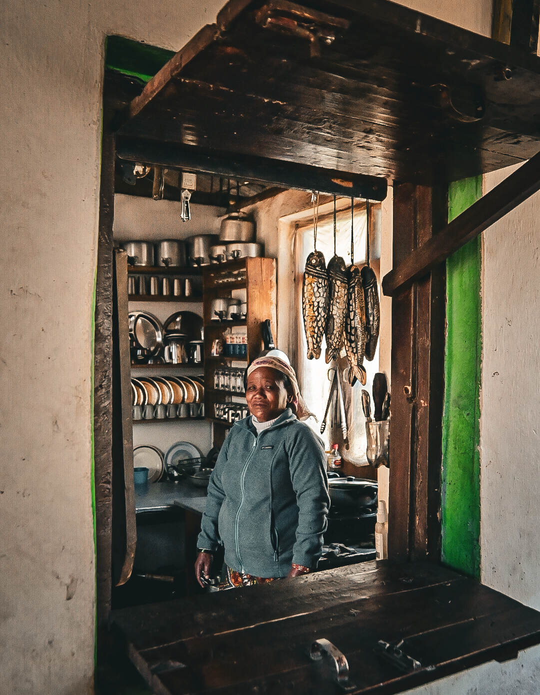 Teahouse cook standing in her kitchen doorway with dried fish hanging above