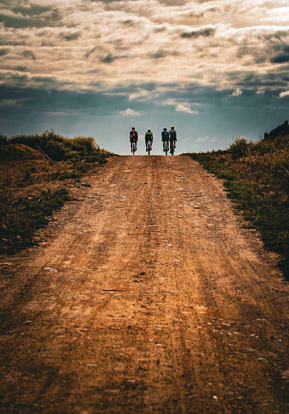 Four riders cresting a gravel climb under heavy cloud