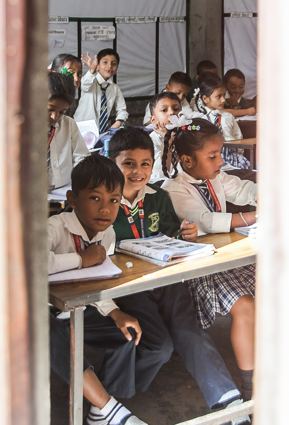 Children smiling at their desks in a classroom, framed through a doorway