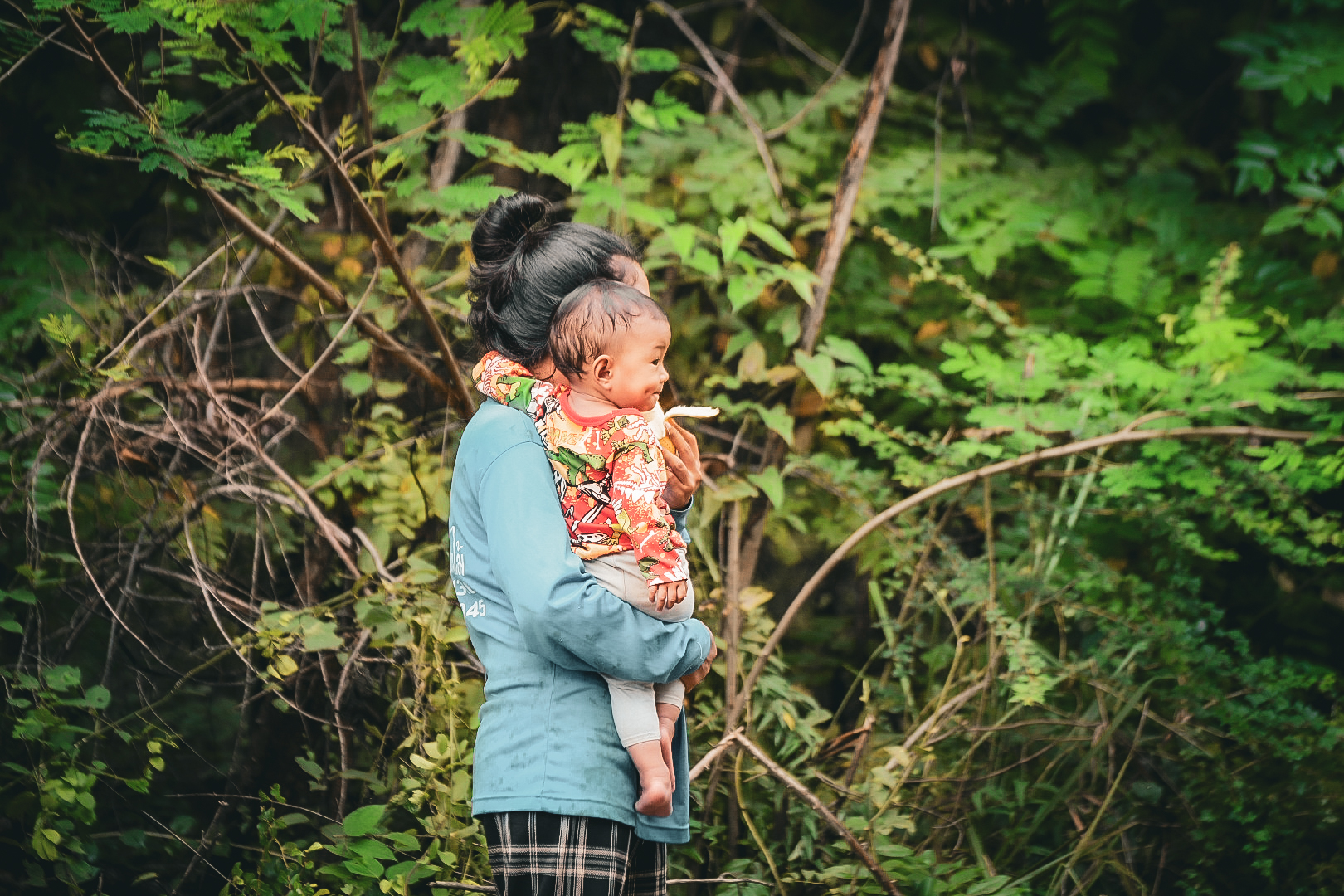 Woman carrying her baby at the roadside in dense green forest