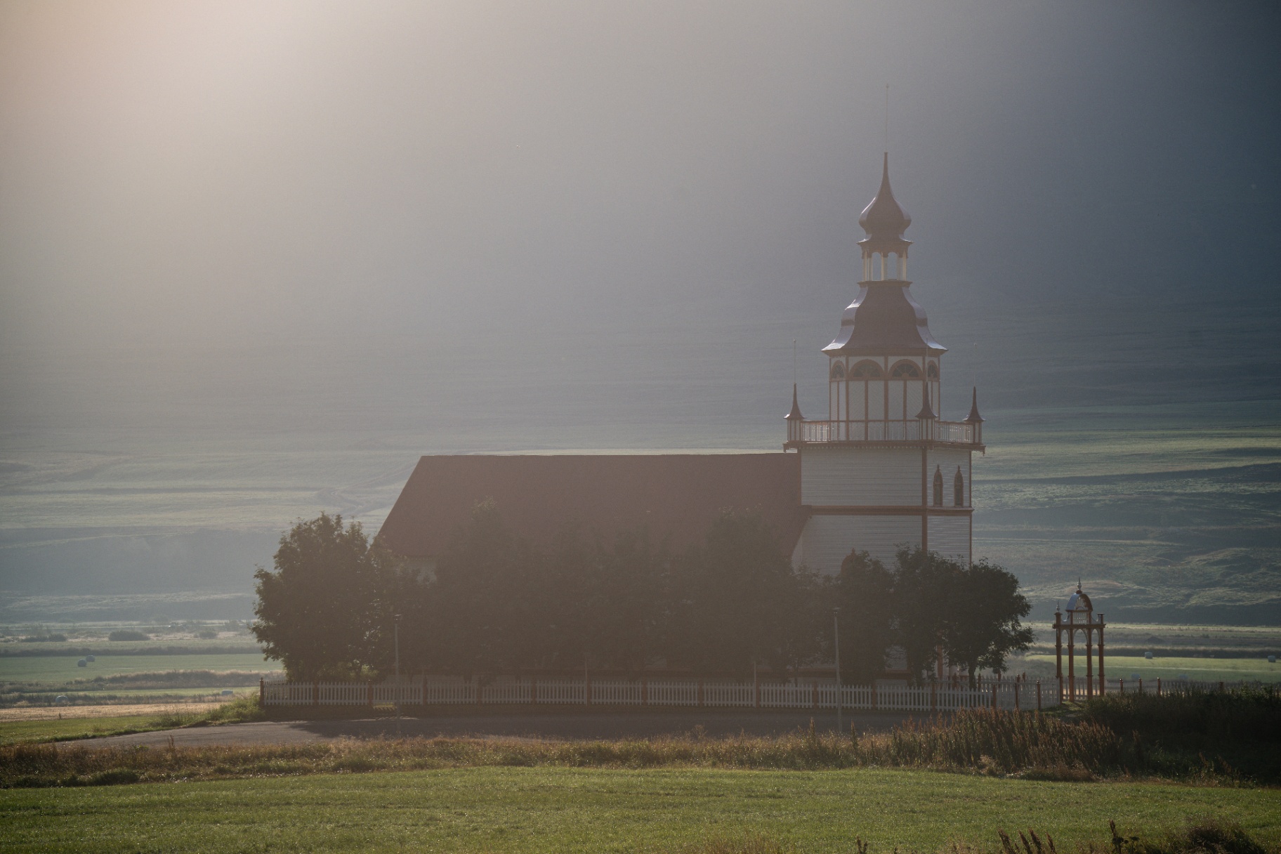 Icelandic church silhouetted in low morning mist above a wide valley
