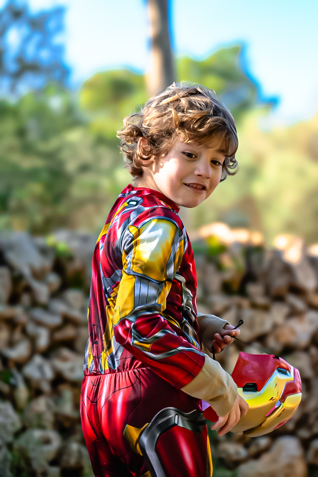Young boy in a superhero suit holding his mask, looking back at the camera
