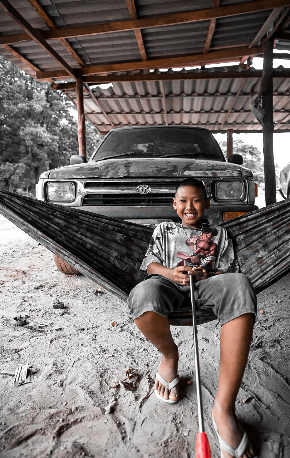 Young boy smiling in a hammock beside a pickup truck under a shelter