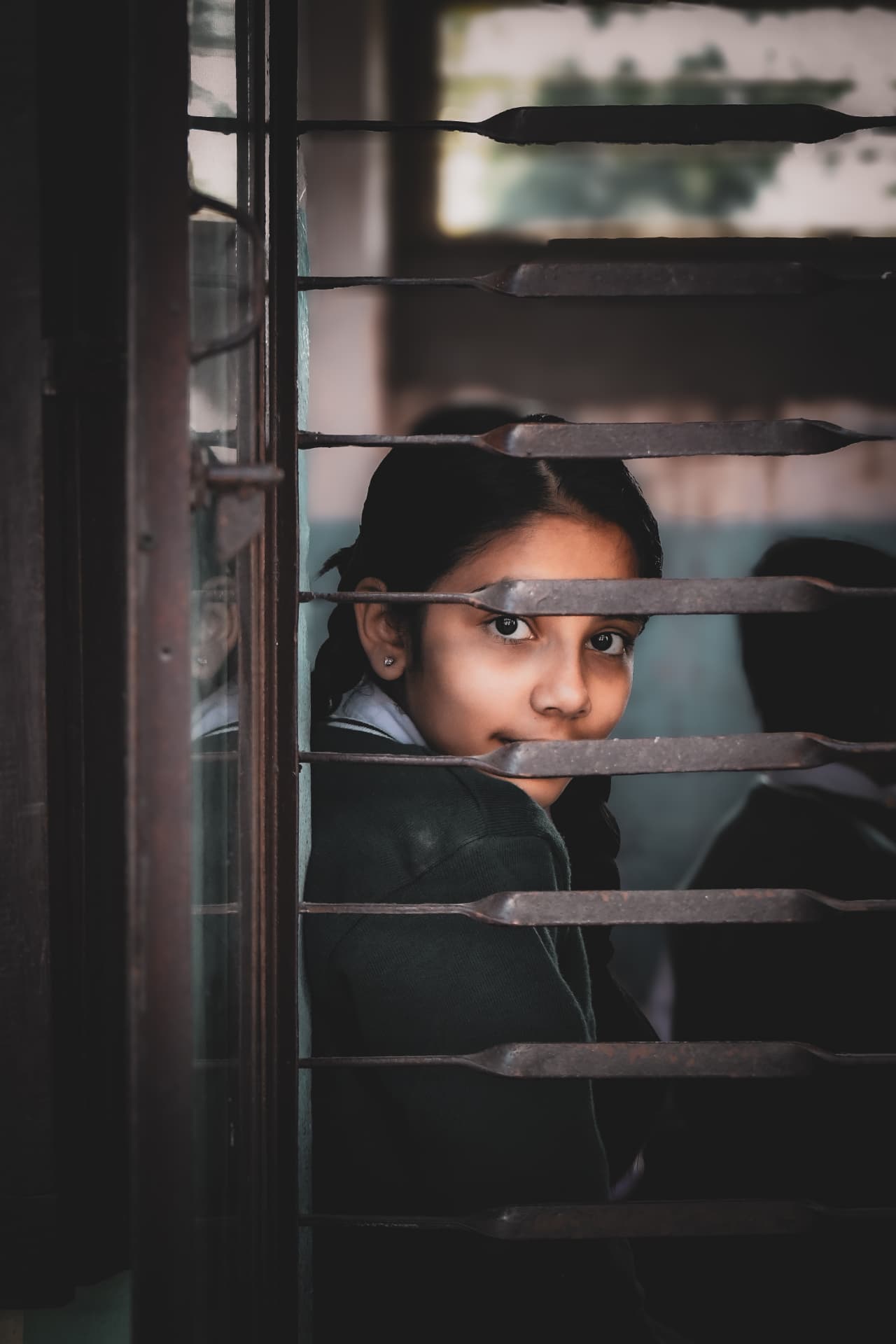 Schoolgirl looking out through a barred classroom window